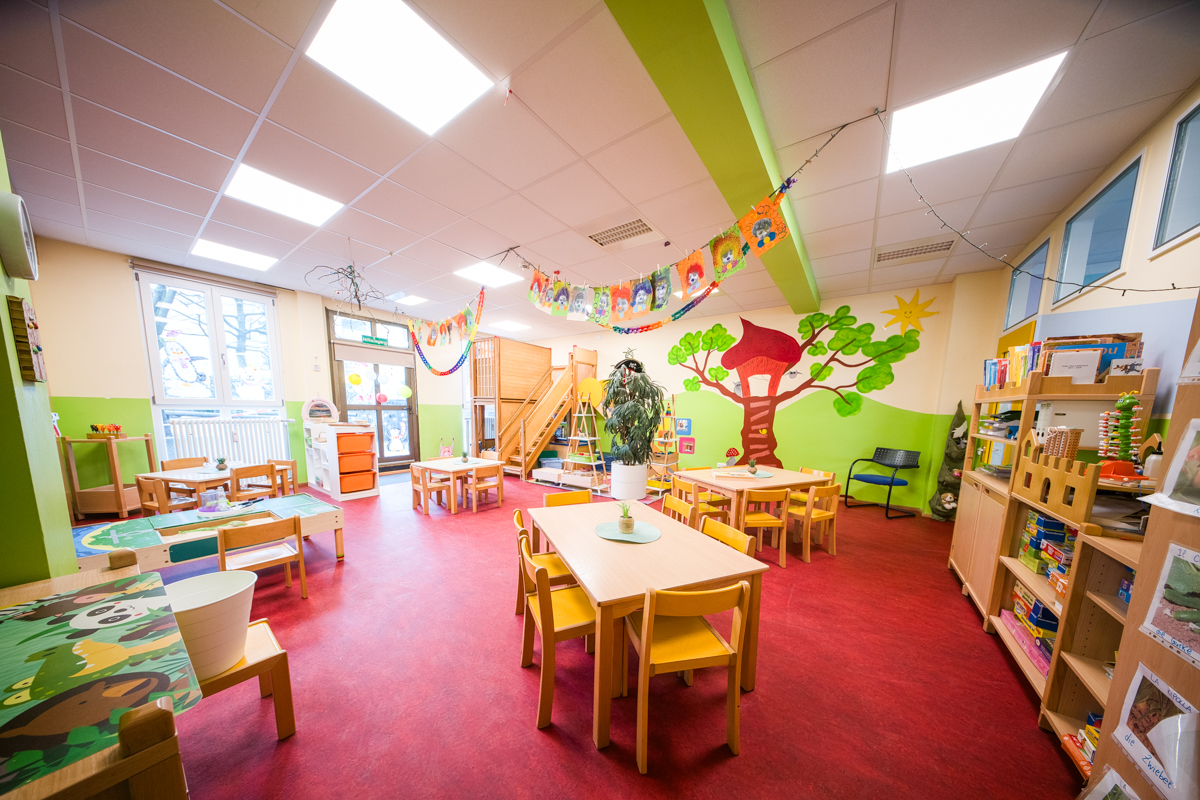 Heller Gruppenraum im Kinderhaus Robinson mit Spielhaus und buntem Baum-Wandbild
